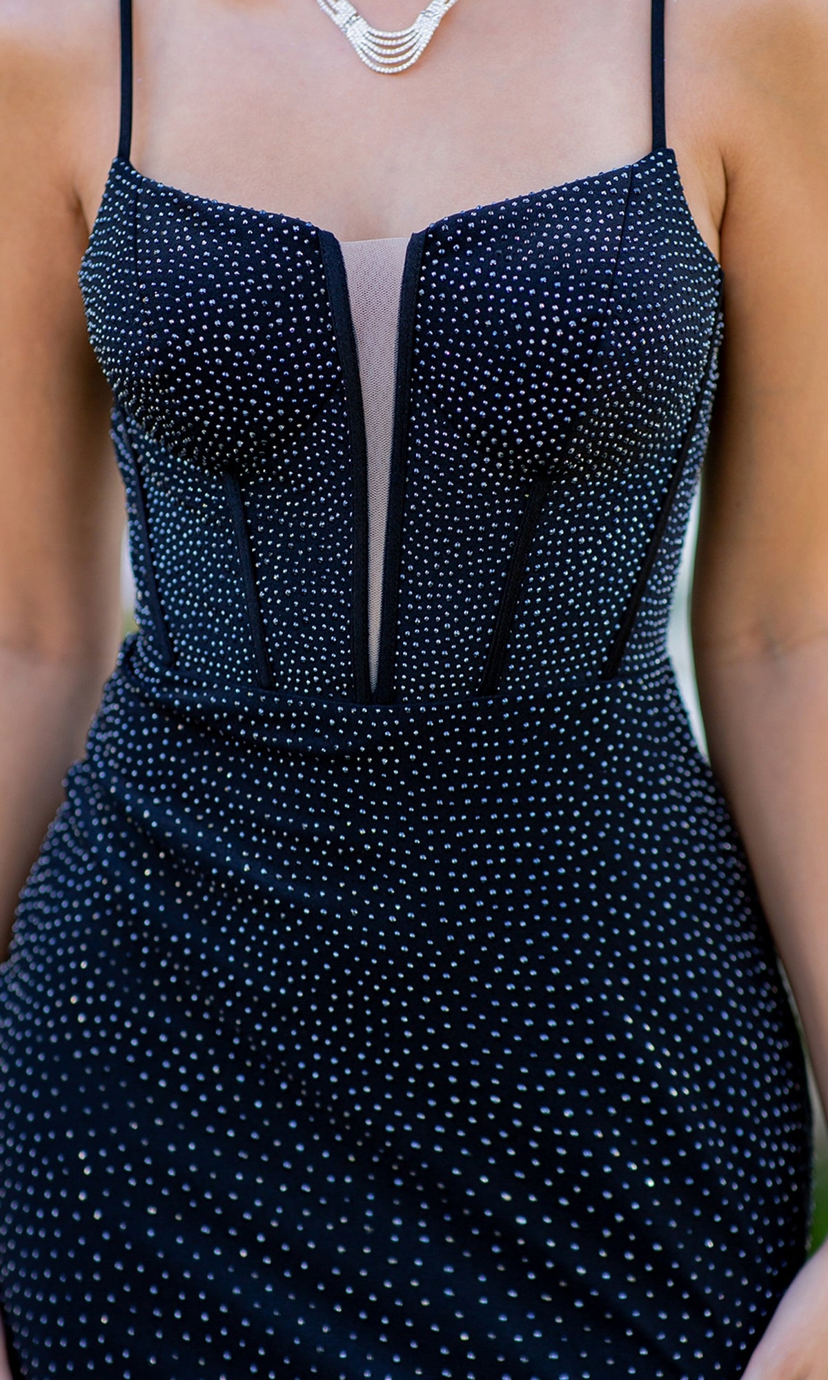 A person wears the Cinderella Couture 8084J Corset Beaded Prom Dress—sleeveless, black with thin straps, mesh panel, small white dots, a chic corset bodice—accessorized with a layered necklace.